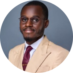 Professional headshot of a man wearing glasses, a beige blazer, and burgundy tie against a blue-gray background.