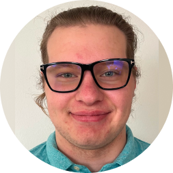 Portrait of a person wearing black-framed glasses and a teal shirt against a neutral beige background.