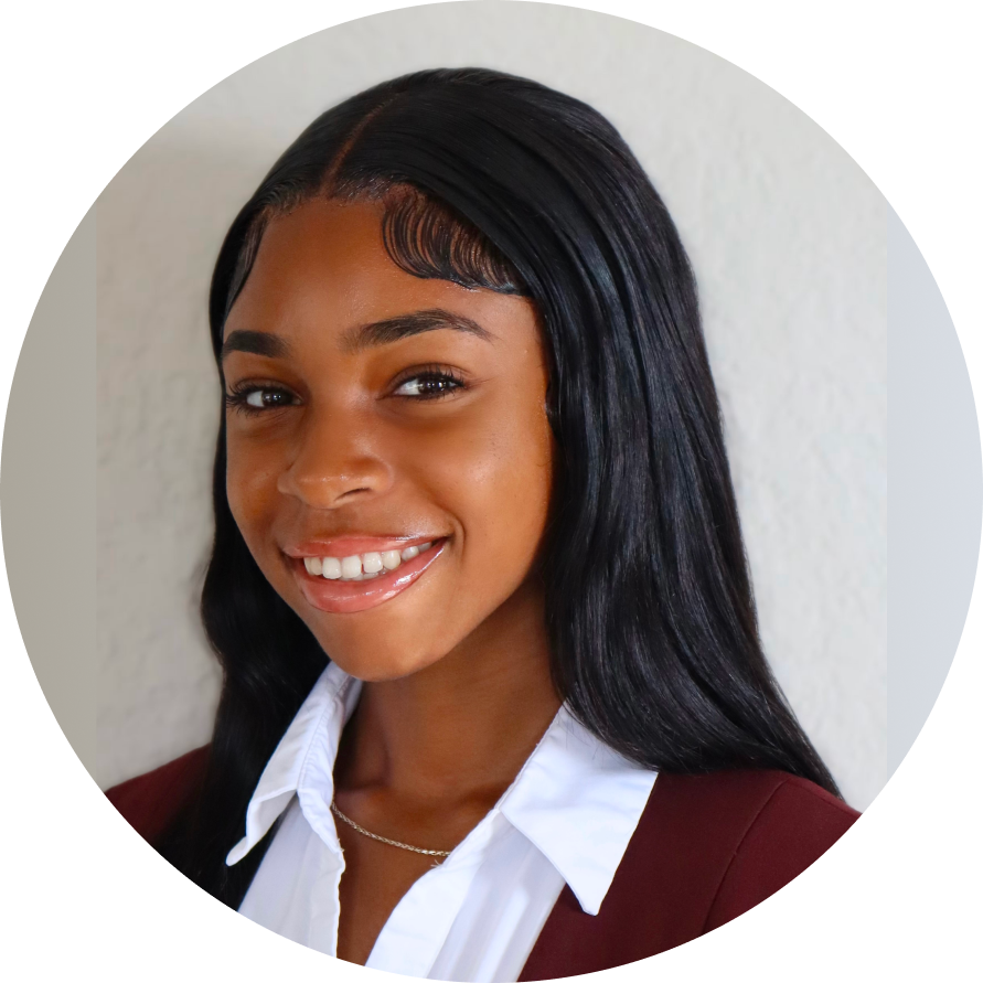 Professional headshot of a woman with long black hair wearing a burgundy blazer and white collared shirt, smiling at the camera against a light background.