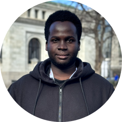 Portrait of a man wearing a black zip-up hoodie against an urban building background.