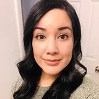 Portrait headshot of a woman with long dark hair wearing a gray sweater against a light background.