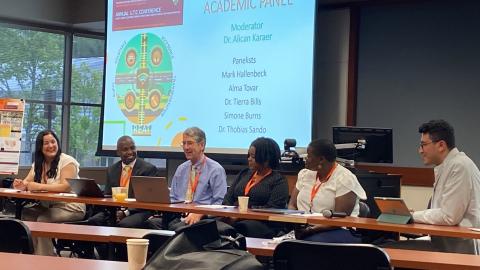 Six panelists seated at a table during an Academic Panel discussion at the Annual UITC Conference, with a presentation slide displayed on screen behind them.
