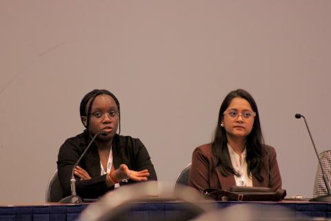 Two panelists seated at a conference table with microphones and name badges, speaking at what appears to be an academic or professional panel discussion.