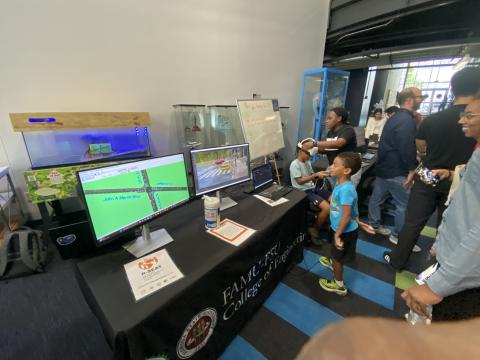 College of Engineering exhibit booth with interactive displays showing virtual reality headset demonstration and mapping software on monitors, with visitors gathered around.