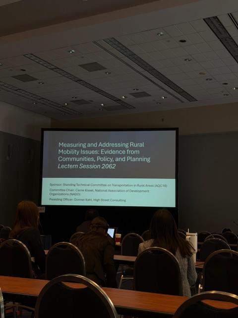 Conference room with attendees viewing a projection screen displaying "Measuring and Addressing Rural Mobility Issues" presentation details for Lectern Session 2062.