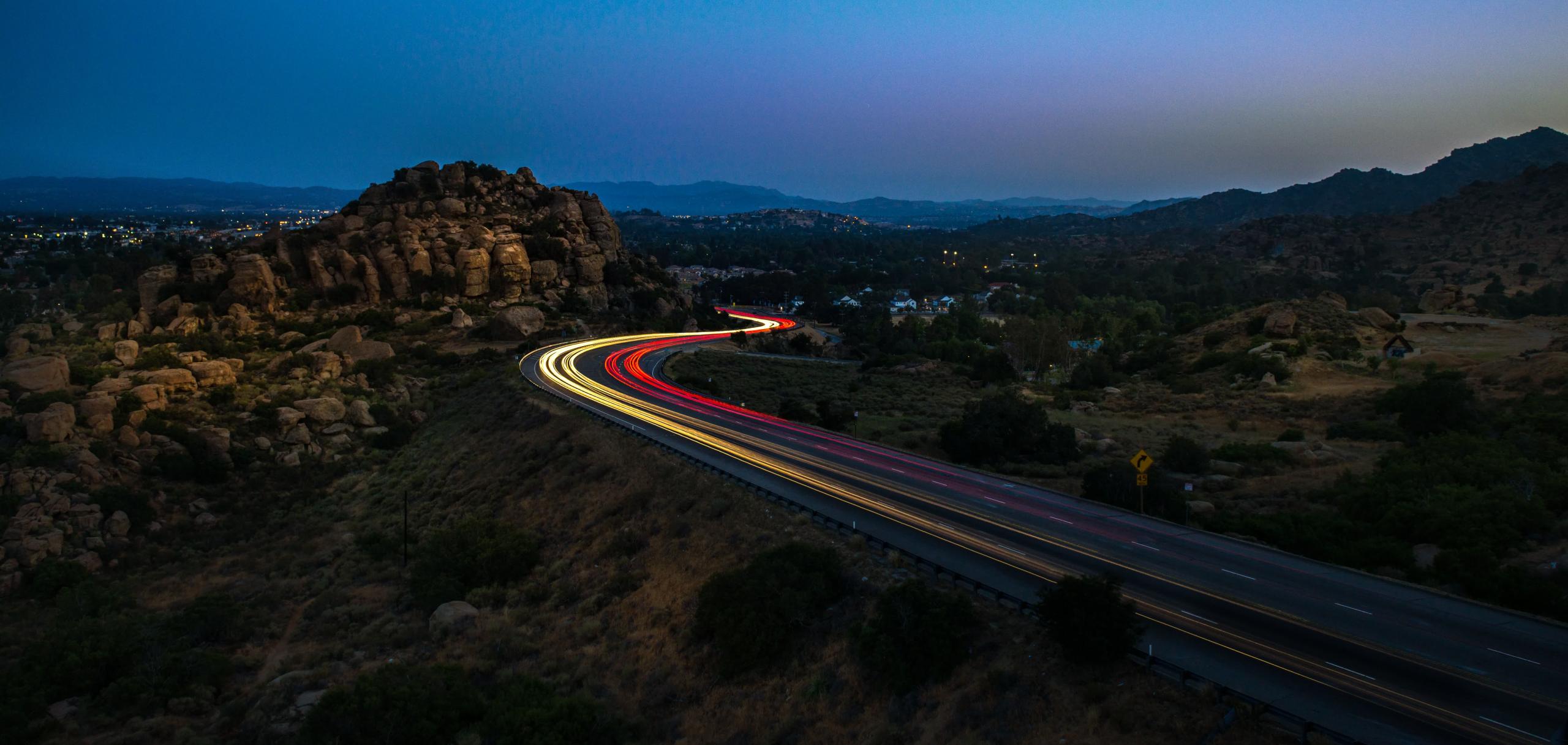 View of a road passing through mountains. On the road is the motion blur of car lights