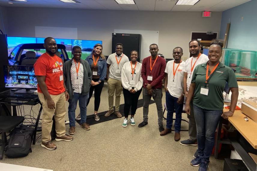 Nine people wearing lanyards stand in a classroom with computer equipment and displays, posing for a group photo.