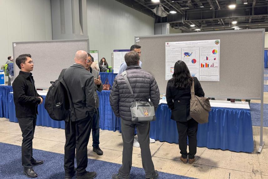 Visitors examine a research poster at an academic conference or poster session in a convention center hall with blue-draped tables.