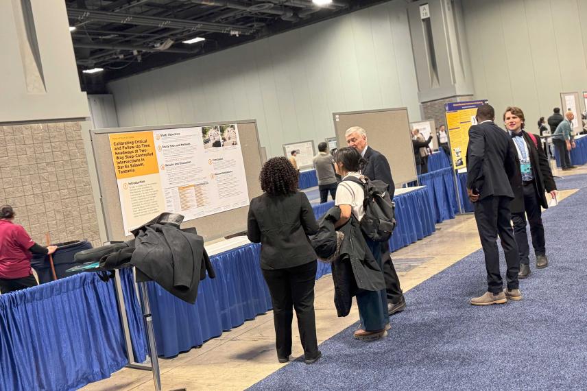 Attendees view research posters at an academic conference in a large hall with blue-draped tables and displayed presentation boards.