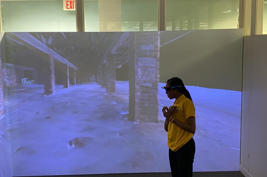 Person in yellow shirt standing before large projection display showing an urban underpass scene in blue tones within a modern glass-walled room.