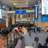 Large convention center atrium with crowds of attendees, blue registration signage, and corporate sponsor logos displayed on walls and digital screens.